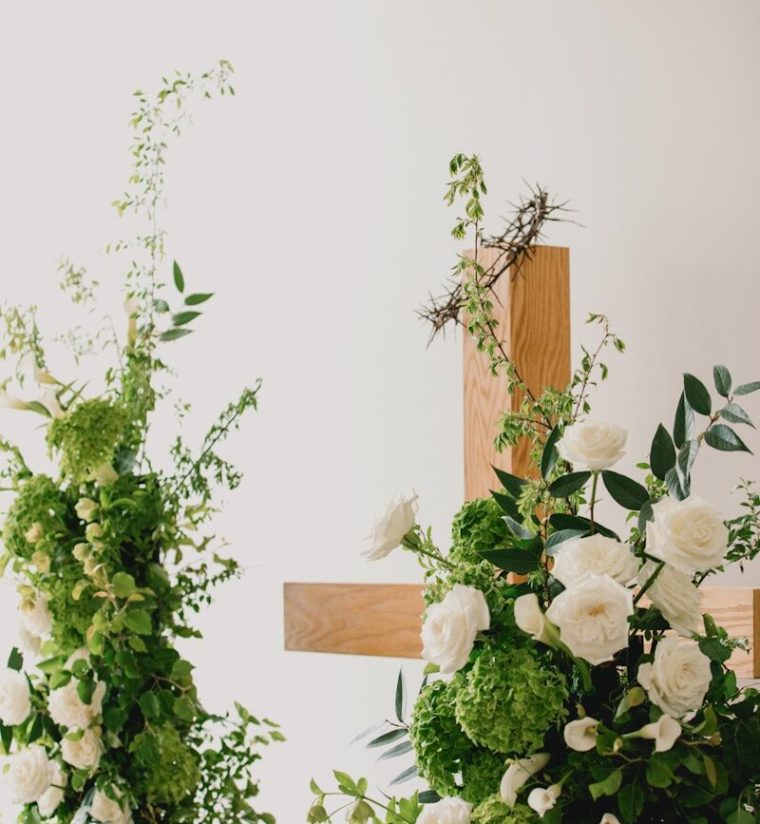 Wooden cross adorned with white roses and greenery